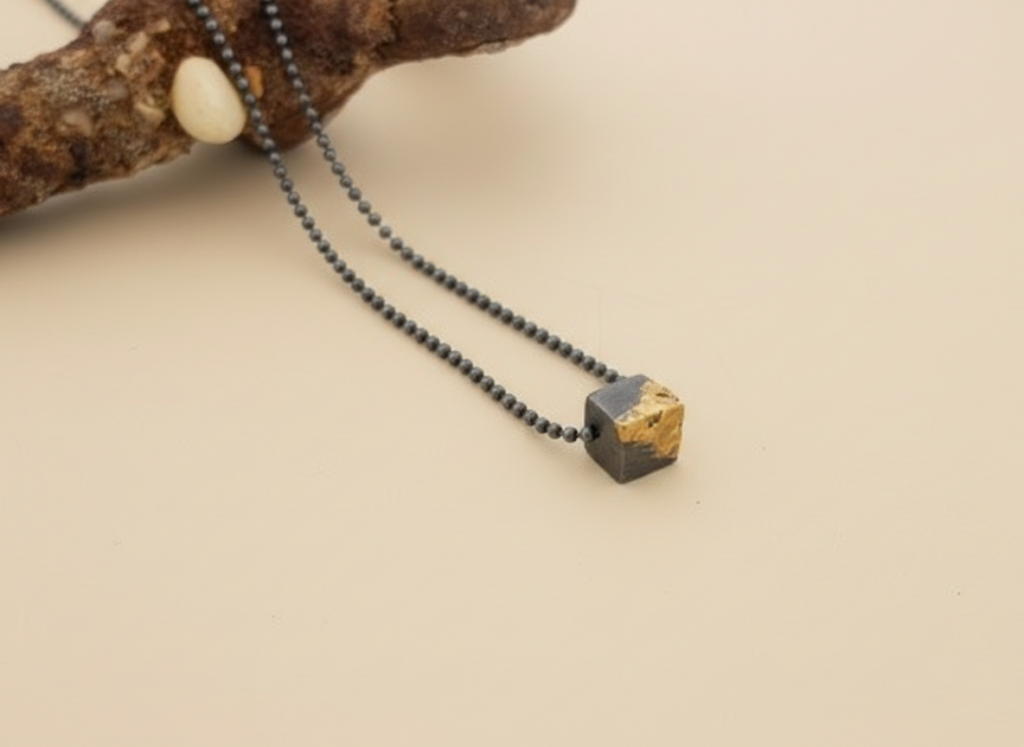 שרשרת כסף מושחר עם קוביית זהב טהור בעבודת יד על רקע קרם של סטודיו צורפות פלוס