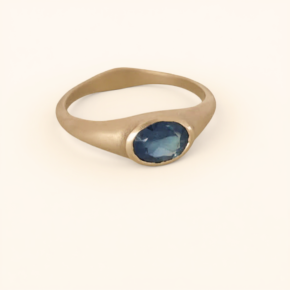 טבעת זהב 18 קראט בעבודת יד משובצת אבן ספיר כחולה אובלית, על רקע בהיר.