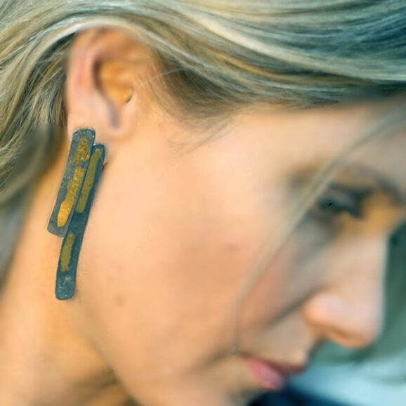 עגילים ארוכים מכסף מושחר עם פס זהב בעבודת יד על רקע קרם של סטודיו צורפות פלוס